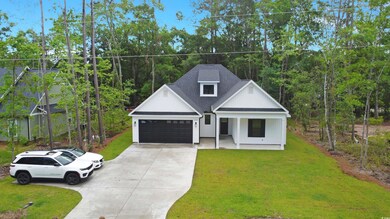 Zoomed-out view of this traditional, farmhouse-inspired home featuring concrete driveway, and attached garage, a front yard, covered porch, and roof with shingles