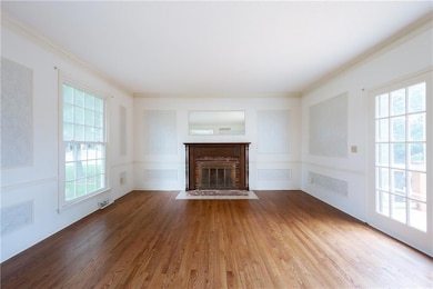 Formal iving room with a brick fireplace, wood finished floors, ornamental molding, and plenty of natural light with fixed French doors.
