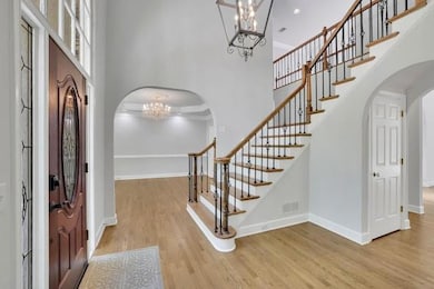 Entrance foyer with wood finished floors, arched walkways, an inviting chandelier, a high ceiling, and visible vents