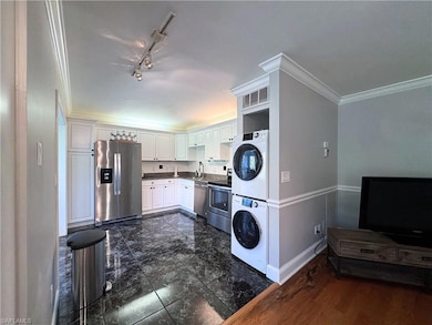 Kitchen featuring stainless steel appliances, stacked washer / dryer, crown molding, baseboards, and white cabinets