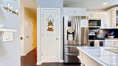 Kitchen featuring appliances with stainless steel finishes, glass insert cabinets, white cabinetry, light stone counters, and decorative backsplash
