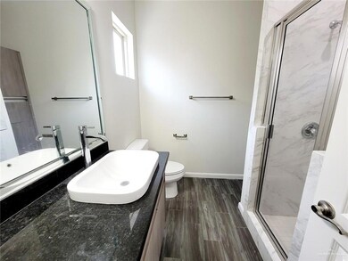 Bathroom featuring toilet, wood finish floors, vanity, baseboards, and a marble finish shower