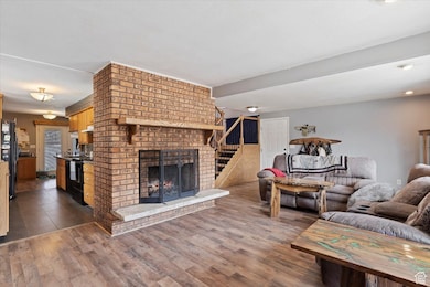 Living room featuring dark wood-type flooring, stairs, and a brick fireplace