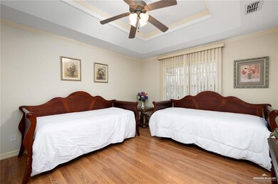 Bedroom featuring a raised ceiling, wood finished floors, ornamental molding, and ceiling fan