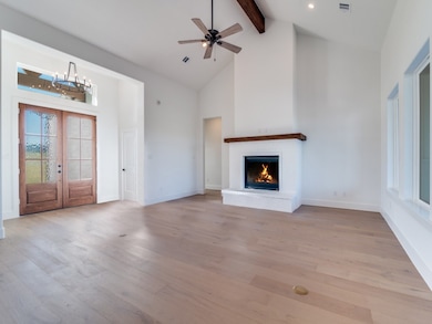 Unfurnished living room featuring high vaulted ceiling, french doors, light wood-style floors, beam ceiling, and a fireplace