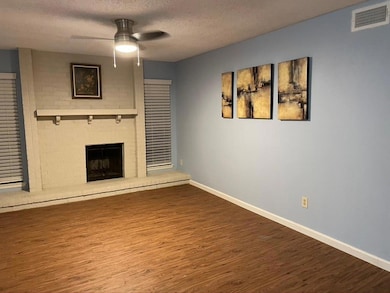 Unfurnished living room with a textured ceiling, wood finished floors, a ceiling fan, and a brick fireplace