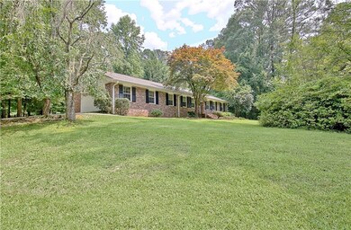 Ranch-style home featuring brick siding, a front lawn, roof with shingles, and covered porch