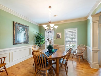 Dining room featuring decorative columns, light wood-style floors, a chandelier, a decorative wall, and ornamental molding