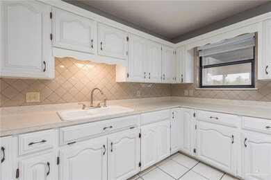 Kitchen featuring a sink, light tile patterned floors, light countertops, tasteful backsplash, and white cabinetry