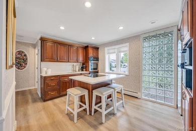 Kitchen featuring wallpapered walls, a breakfast bar, brown cabinetry, light wood-style flooring, and stainless steel oven