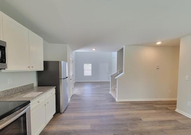 Kitchen with white cabinets, light stone countertops, stainless steel appliances, and light wood-type flooring