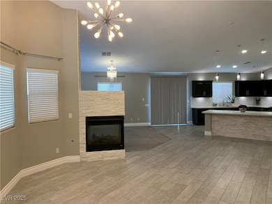 Kitchen with dark cabinetry, open floor plan, decorative light fixtures, a fireplace, and backsplash