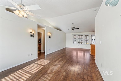Unfurnished living room with a ceiling fan, dark wood-style flooring, vaulted ceiling, and a textured ceiling