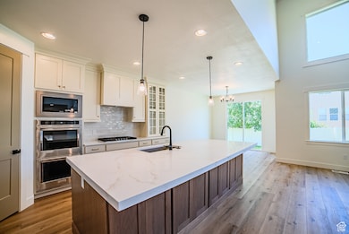 Kitchen with recessed lighting, tasteful backsplash, light wood-style flooring, glass insert cabinets, and hanging light fixtures