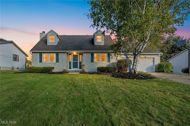 Cape cod home featuring a front lawn, a chimney, driveway, and a garage