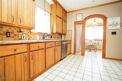 Kitchen with brown cabinets, tasteful backsplash, ornamental molding, light tile patterned floors, and stainless steel dishwasher