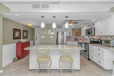 Kitchen with stainless steel appliances, decorative light fixtures, a center island, white cabinetry, and recessed lighting