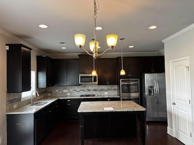 Kitchen featuring appliances with stainless steel finishes, light stone countertops, a kitchen island, a chandelier, and crown molding