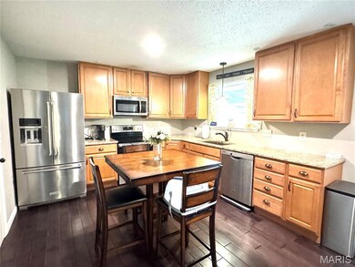 Kitchen featuring stainless steel appliances, dark wood-type flooring, a textured ceiling, decorative light fixtures, and light stone counters