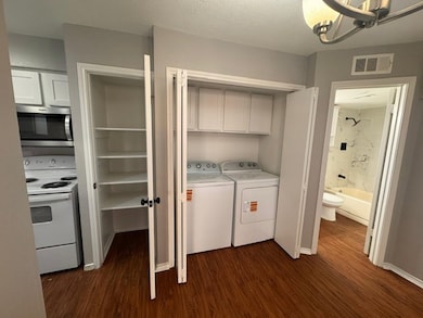 Laundry area with dark wood-type flooring, a chandelier, washer and dryer, and a textured ceiling
