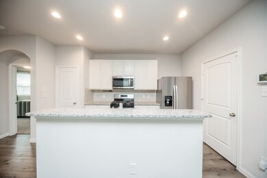 Stainless steel appliances, white cabinetry, and granite countertops, featuring ample lighting and a view into the living area.