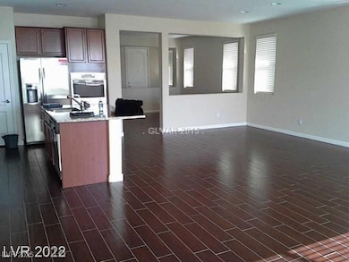 Kitchen with appliances with stainless steel finishes, open floor plan, a kitchen island with sink, light stone countertops, and dark wood-type flooring