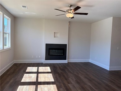 Unfurnished living room featuring a tiled fireplace, dark wood finished floors, and ceiling fan