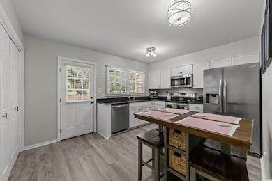 Kitchen featuring stainless steel appliances, dark countertops, white cabinets, light wood-style floors, and a sink