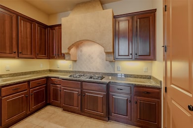 Kitchen featuring light tile patterned flooring, tasteful backsplash, stainless steel gas cooktop, and light stone countertops
