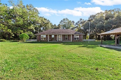 Ranch-style home featuring a front lawn, brick siding, and view of wooded area