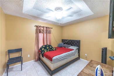 Tiled bedroom with a textured ceiling, a tray ceiling, and ceiling fan