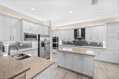 Kitchen with a kitchen island, wall chimney range hood, stainless steel appliances, sink, and light stone countertops