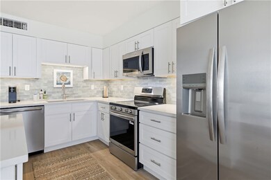 Kitchen with appliances with stainless steel finishes, white cabinetry, tasteful backsplash, and light wood-type flooring