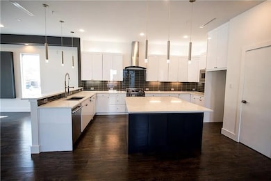 Kitchen featuring a peninsula, backsplash, white cabinets, pendant lighting, and dark wood-style floors