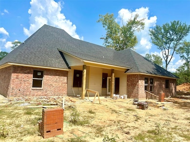 View of front facade with a shingled roof, a patio, and brick siding