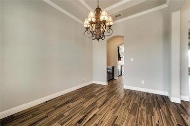 Unfurnished room with a chandelier, dark wood-style floors, baseboards, visible vents, and arched walkways