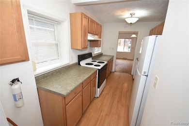 Kitchen with white appliances, light wood-type flooring, a textured ceiling, hanging light fixtures, and under cabinet range hood