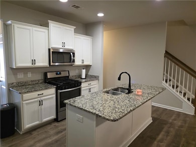 Kitchen with appliances with stainless steel finishes, white cabinets, dark wood finished floors, light stone countertops, and recessed lighting