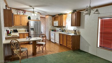 Kitchen with white appliances, a ceiling fan, light countertops, brown cabinets, and light wood-style flooring