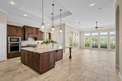 Your well-lit kitchen contains modern stainless steel appliances, dark wood cabinetry, and a large central island. The room features high ceilings with recessed lighting, pendant lights, and a tile floor that extends into an open living area with ample natural light from large windows.