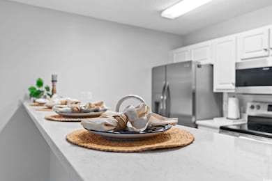 Kitchen featuring stainless steel appliances, white cabinets, and light stone countertops