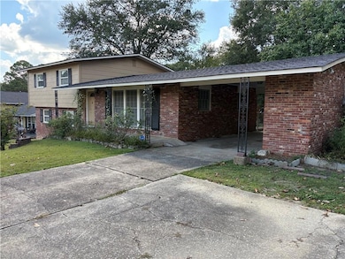 Split level home featuring brick siding, a front yard, driveway, a carport, and covered porch