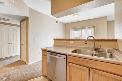 Kitchen with dishwasher, light brown cabinetry, light countertops, light colored carpet, and light tile patterned floors