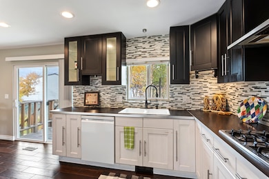 Kitchen featuring glass insert cabinets, dishwasher, range hood, decorative backsplash, and recessed lighting. Slider going to backyard and deck