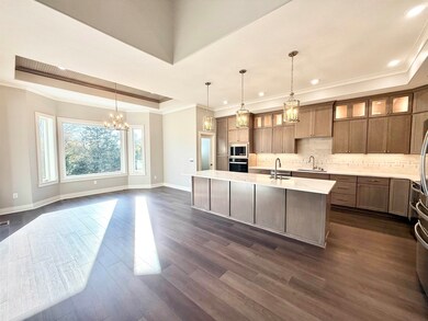 Kitchen with a raised ceiling, backsplash, glass insert cabinets, decorative light fixtures, and an island with sink