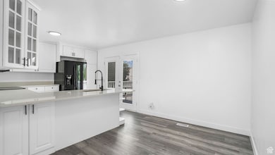 Kitchen with black refrigerator with ice dispenser, glass insert cabinets, light countertops, white cabinets, and dark wood-style flooring