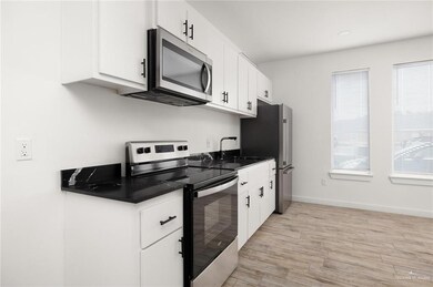 Kitchen with appliances with stainless steel finishes, dark countertops, white cabinetry, and light wood-type flooring