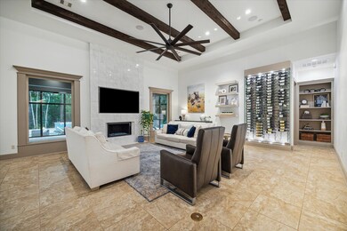 Living room with custom display wine vault, eye-catching ceiling beams, gas fireplace w/fire glass + large picture windows overlooking the pool.