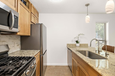 Kitchen with appliances with stainless steel finishes, tasteful backsplash, light stone counters, decorative light fixtures, and a textured ceiling