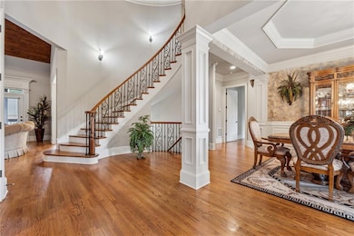 Dining room featuring crown molding, wood finished floors, stairway, a decorative wall, and ornate columns